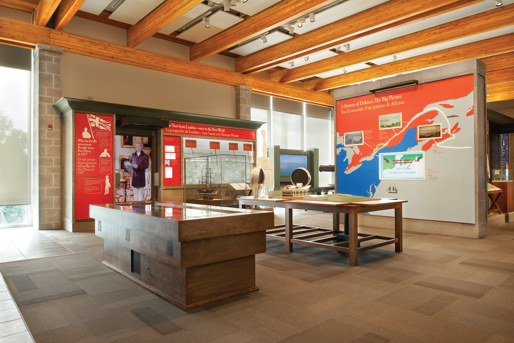 Exhibit space with floor and wall displays, stone wall on left and wood rafter ceilings