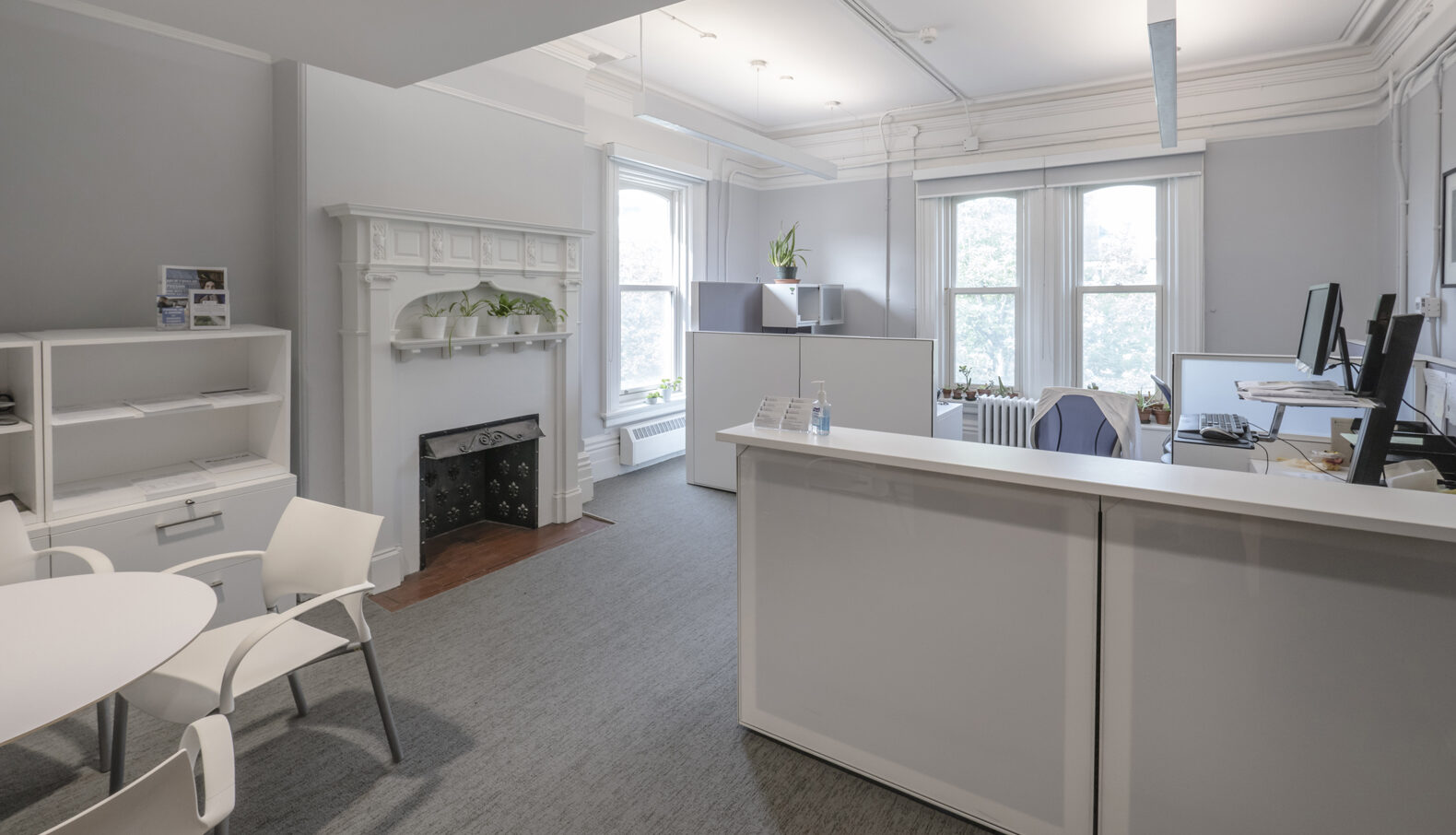 All white private office with fireplace, workstation, guest seating, shelving, large windows, and dropped fluorescent lighting
