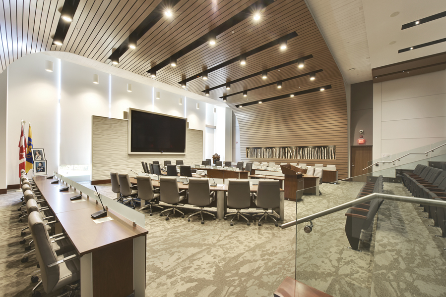 Council chamber with semi circle council seats in centre, table seating on left and gallery seating on right and curved wood planked wall ceiling feature