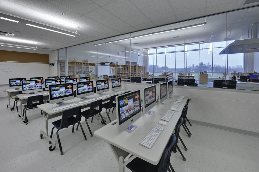 Computer lab with Mac workstations, glazed curtain wall with views into library continuing on through exterior windows to trees