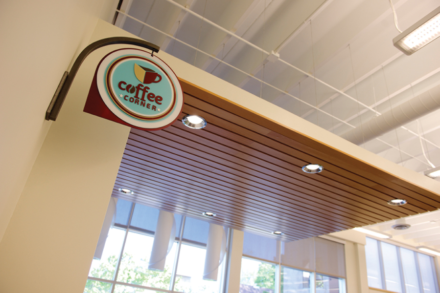 Coffee Corner sign looking up to wood plank ceiling feature, dropped fluorescent lighting, white pendant lighting and large windows