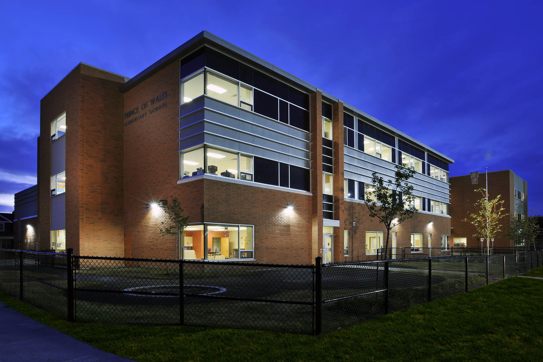 Illuminated three storey red brick school with sconce lighting, windows and steel detail at dawn