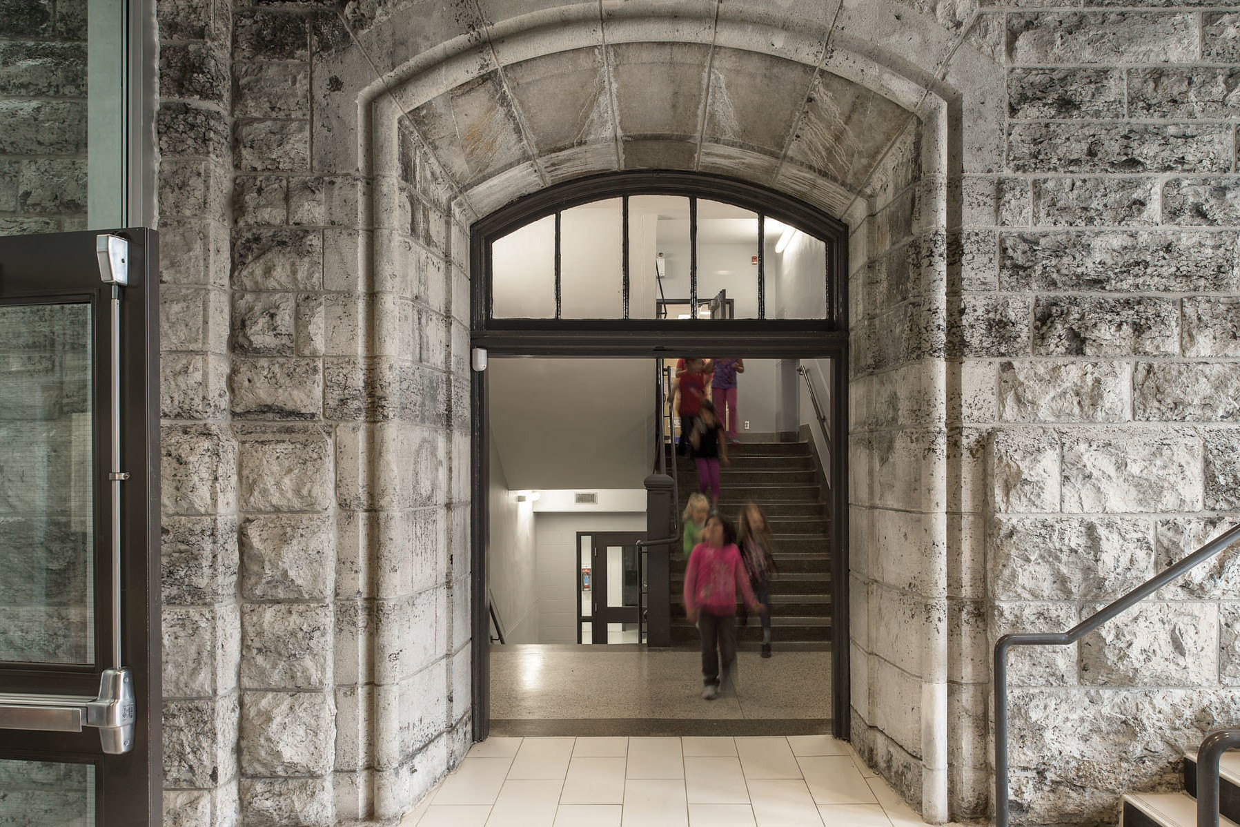 View of students in stairwell through archway in original stone façade from corridor in new addition