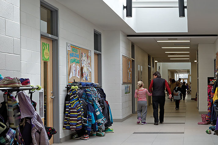 Students walk down hallway with large skylight and coat racks on left