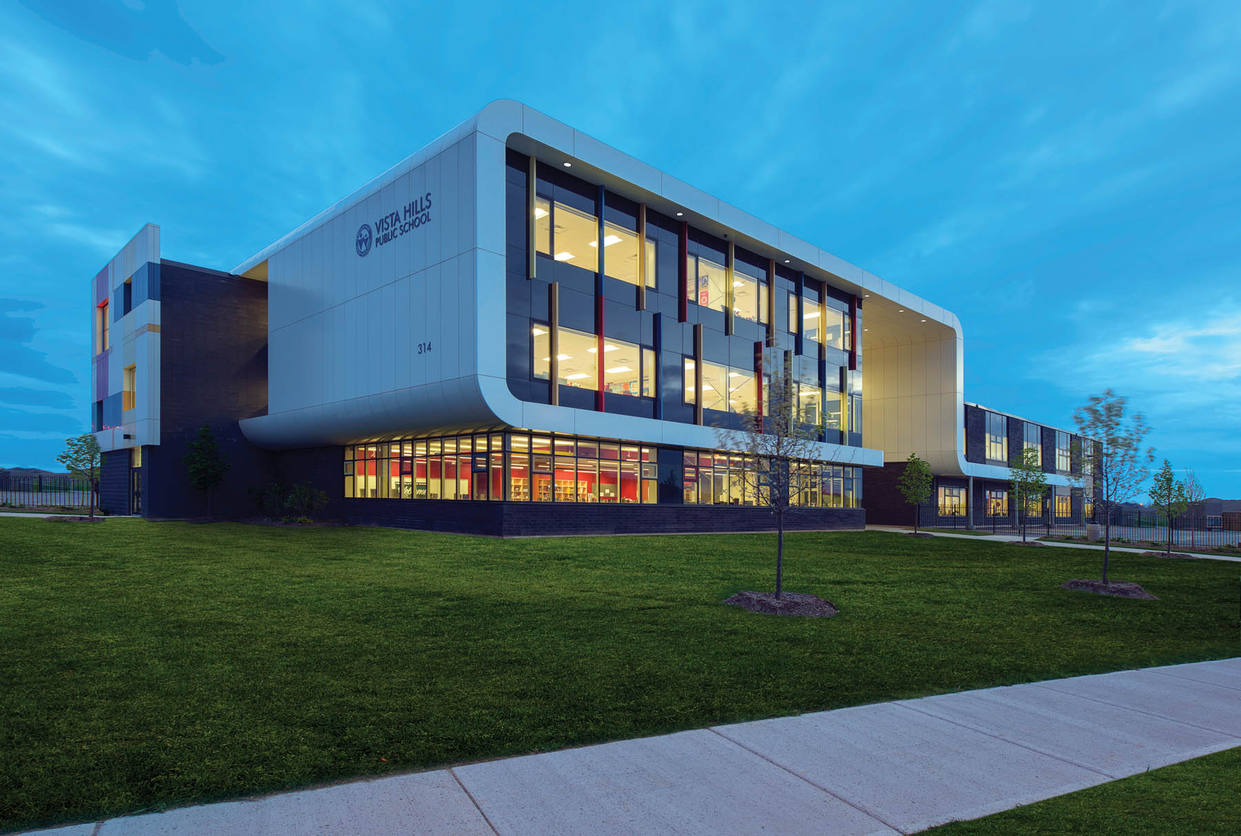 Front façade of three storey school with white framing and vertical colour block details across windows at dusk