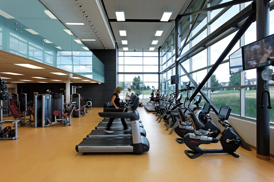 Glazed double height fitness area with treadmills and exercise bikes and second storey corridor with glass guard rail