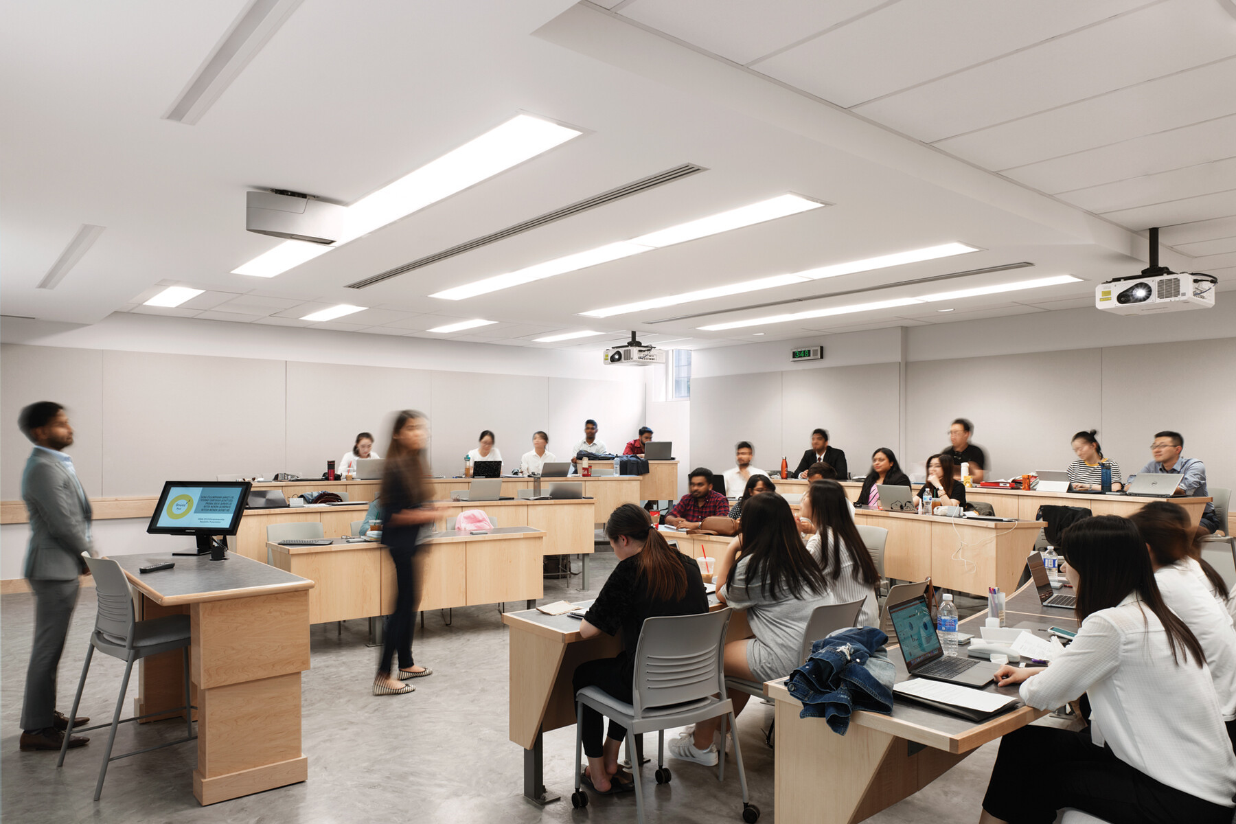 Student filled lecture room with four tiers of flexible wood seating and white walls