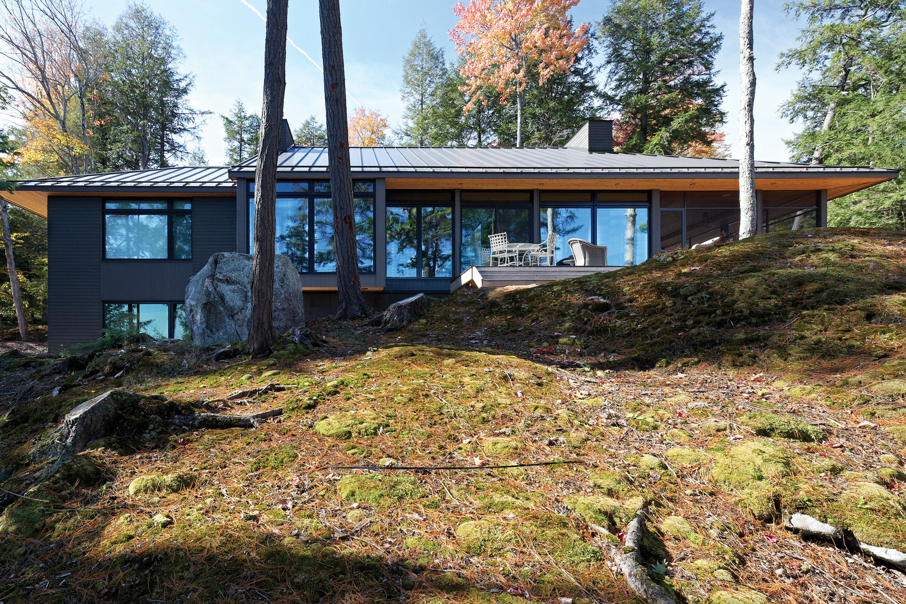 Elevation of cottage with trees reflected in windows and rugged landscape in foreground