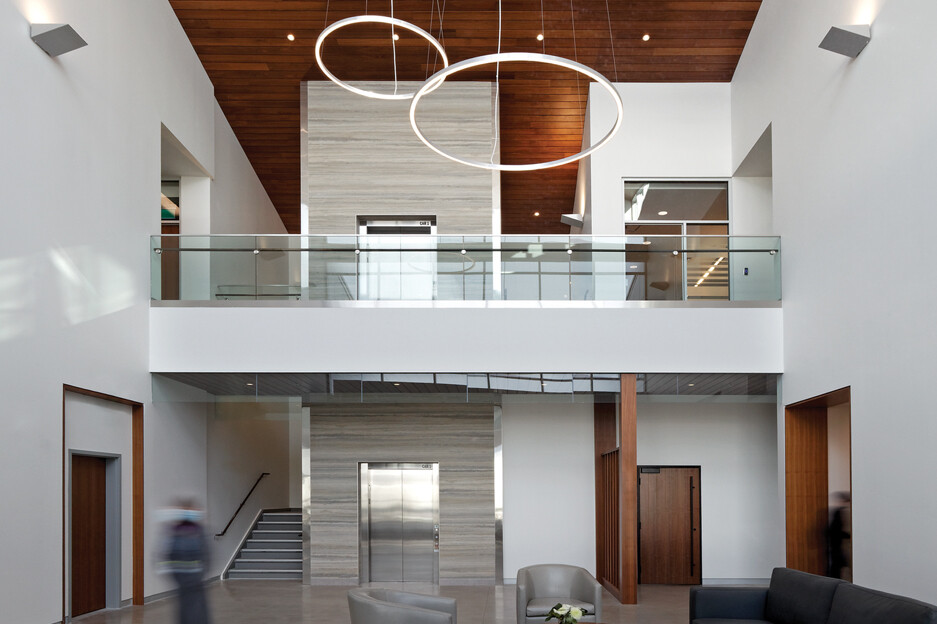 Double height entry lobby with white walls and wood slat ceiling with ring light fixtures