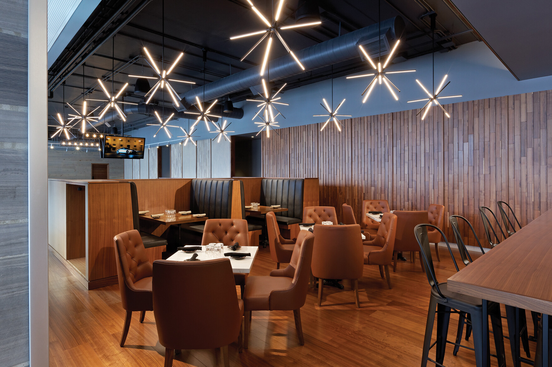 Bar lounge seating with white square tables and tan chairs, black booth seating and star burst light fixtures